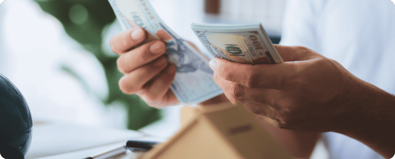Person counting a stack of hundred-dollar bills.