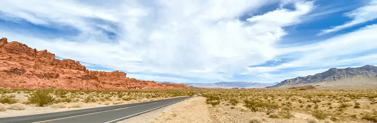 Open road stretching through Nevada's desert with red rock formations and blue skies.