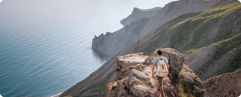 A traveler with a backpack standing on a cliff overlooking the sea, symbolizing the adventurous side of travel CT tech jobs.
