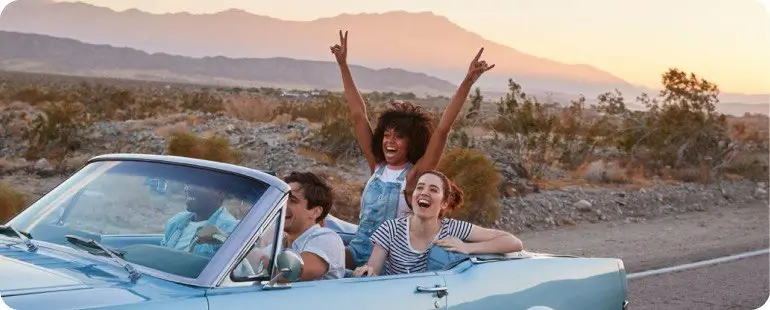 Group of happy travel nurses on a road trip through the desert in a classic convertible.