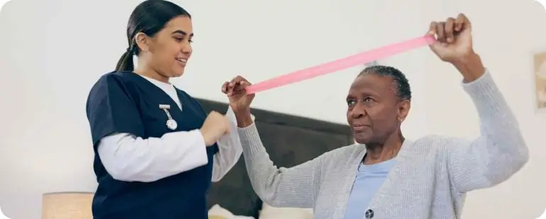 Physical therapist assisting elderly woman with resistance band exercises at home