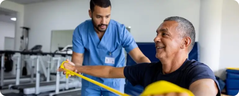 Male physical therapy patient using resistance band under therapist supervision