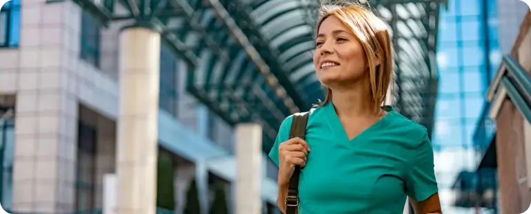 Smiling healthcare professional in scrubs walking outside clinic, symbolizing the freedom of the best travel healthcare jobs