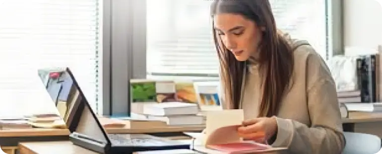 Female student studying for the NPTE physical therapy exam with books and laptop on desk.